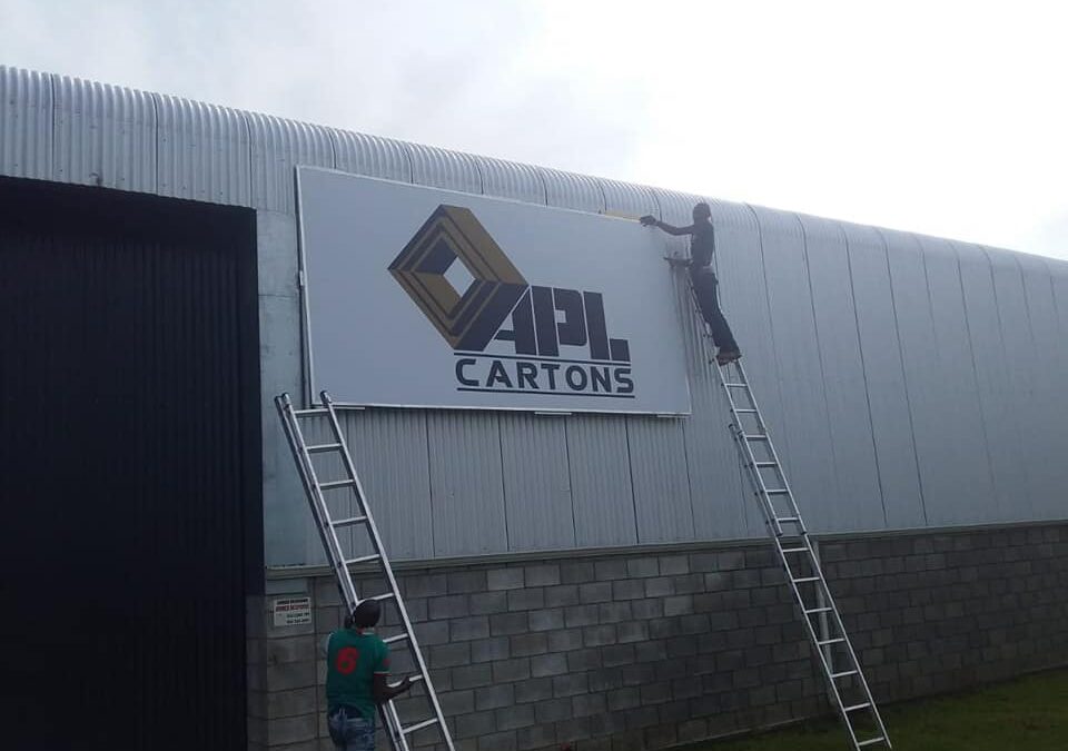 RealXposure team installing a large exterior APL Cartons building sign